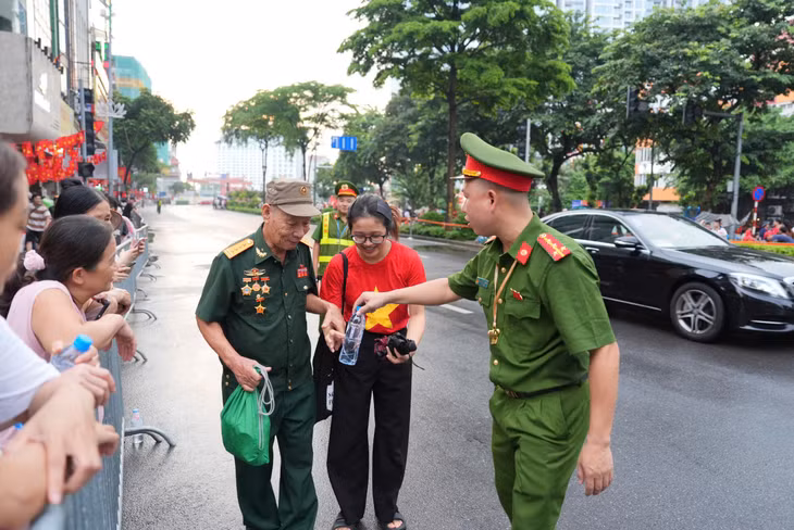 Chiến sĩ công an phát nước, hỗ trợ cựu chiến binh và người dân tại khu vực Kim Mã trong chiều 1.9, đảm bảo mọi người có chỗ ngồi và sức khỏe tốt để chờ xem diễu binh, diễu hành sáng mai 2.9. Ảnh: Huyền Trang - Xuân Hiệp