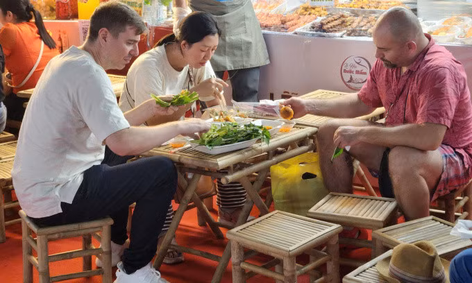 Thomas (áo hồng) thưởng thức bánh căn chấm mắm chua ngọt tại lễ hội tối 23/10. Ảnh: Bích Phương