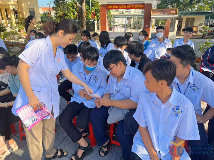 Cán bộ dân số phường Quảng Yên phát tờ rơi tuyên truyền cho học sinh về chăm sóc SKSS vị thành niên, thanh niên. Ảnh: Vân Anh