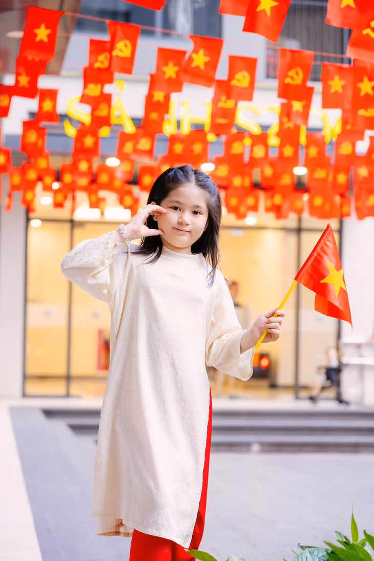 Em nhỏ hạnh phúc đi giữa cờ hoa, tạo dáng chụp hình dưới màu cờ đỏ thắm.
