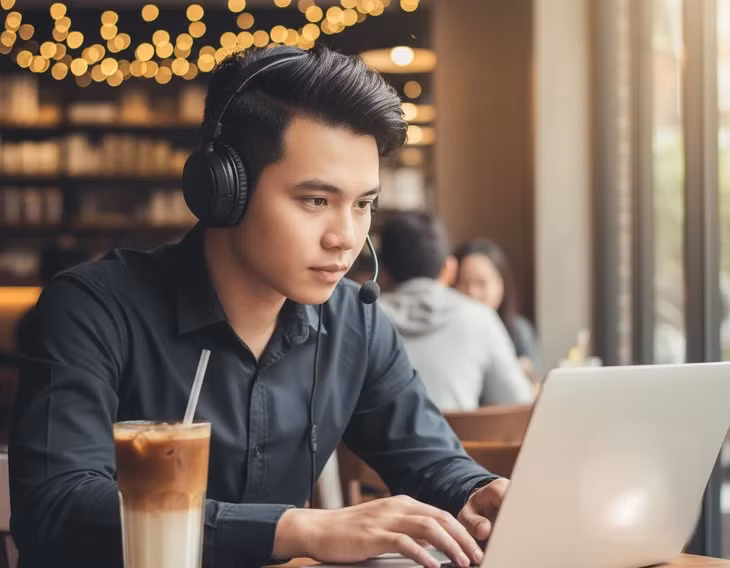 Chàng trai sử dụng micro chống ồn trong tai nghe hỗ trợ họp online ngoài quán cà phê