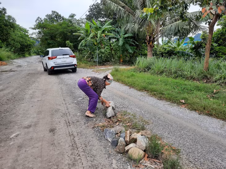 Bà Ng.Th.T (tổ 54, khu 6B) hì hụi vần những hòn đá rơi trên đường để đảm bảo ATGT.