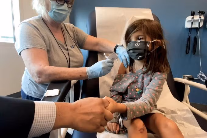 Một bé gái 5 tuổi nắm tay cha khi được tiêm vaccine Pfizer-BioNTech trong thử nghiệm vào tháng 9/2021. Ảnh: Reuters