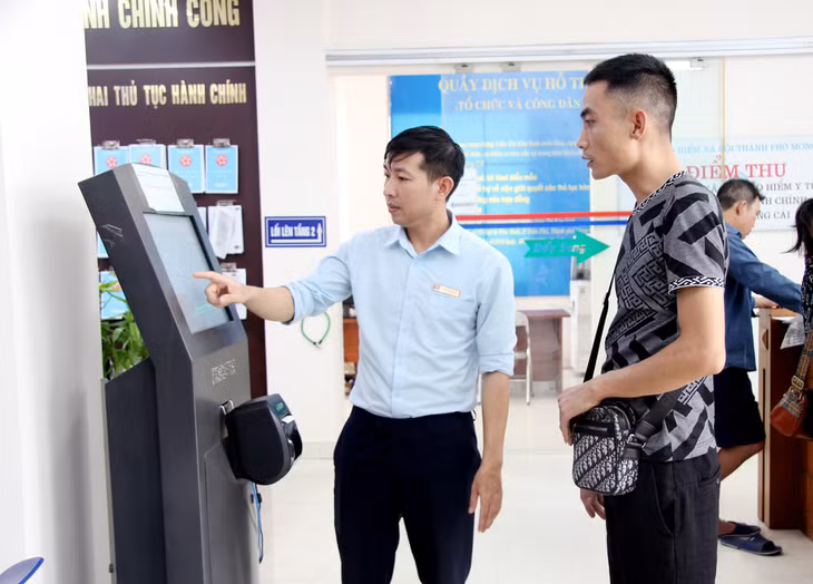 Cán bộ Trung tâm HCC TP Móng Cái hỗ trợ công dân lấy số thứ tự để làm TTHC.