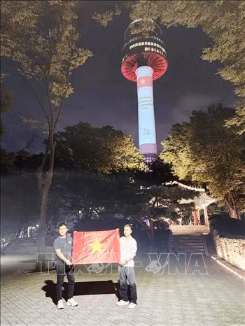 Hai thanh niên Việt Nam tại Hàn Quốc tự hào chụp ảnh bên lá quốc kỳ dưới chân tháp Namsan. Ảnh: Đức Thắng/TTXVN