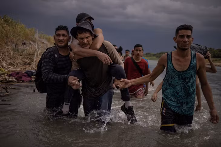 Một người đàn ông cõng người em họ bị tật nguyền lội qua sông Rio Grande, với sự giúp đỡ của 2 người đồng hương ngày 15/9/2023. Ảnh: Reuters