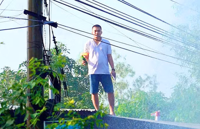 Lê Phước Hoàng, 25 tuổi, con bà Nhan, cố thủ trên nóc nhà cùng chai bom xăng, tấn công lực lượng làm nhiệm vụ, sáng 18/11. Ảnh: Tiến Tầm