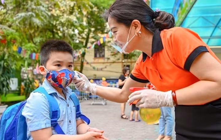Giáo viên đo thân nhiệt cho học sinh trước khi vào lớp. (Ảnh minh hoạ: M.K)