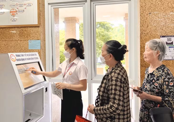 Nhân viên y tế Trung tâm Y tế TX Quảng Yên hướng dẫn người dân lấy số thứ tự đăng ký khám bệnh qua ki-ốt thông minh.