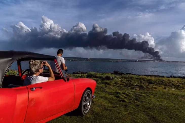 Ngọn lửa lan rộng ở thành phố Matanzas, cách thủ đô Havana 90km về phía đông, nơi có ít nhất 3 thùng dầu thô bốc cháy sau khi bị sét đánh vào đêm thứ 6 vừa qua.Trong ảnh, hai người dân quan sát thấy cột khói khổng lồ bốc lên từ kho nhiên liệu tại thành phố ven biển này. (Ảnh: AP)