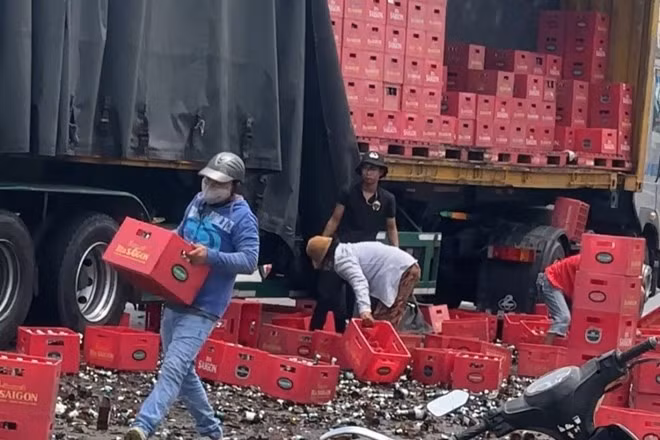 Người dân hỗ trợ thu dọn hiện trường hàng chục két bia từ container rơi vãi xuống đường. Ảnh: An Long