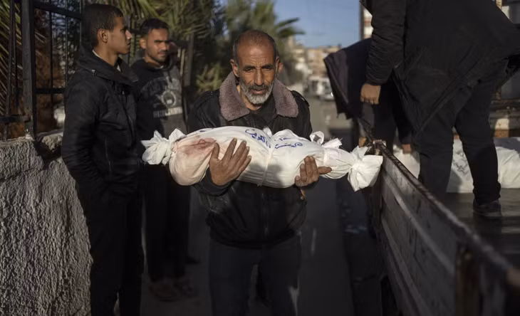 Một người đàn ông Palestine bế thi thể cháu trai thiệt mạng trong vụ pháo kích của Israel vào Dải Gaza ngày 22/12. Ảnh: AP
