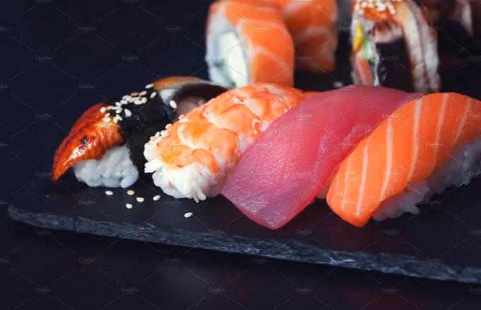 Nigiri sushi: Một trong những loại sushi được biết tới nhiều nhất thế giới là nigiri sushi, chúng làm từ một nắm cơm nhỏ nắm chặt bằng tay sau đó bọc bên trên với trứng hoặc các loại hải sản như tôm, mực, cá, lươn... đôi khi có cuộn thêm một miếng rong biển nhỏ. Món ăn này bắt đầu phổ biến từ thời kỳ Edo (1603 - 1867). Khi ăn Nigiri sushi cần gắp hoặc cầm bằng tay sạch chấm tương, không chấm cơm và tương vì đã trộn gia vị, rồi ăn cả miếng, tránh cắn nửa chừng. Ảnh: Creative Market