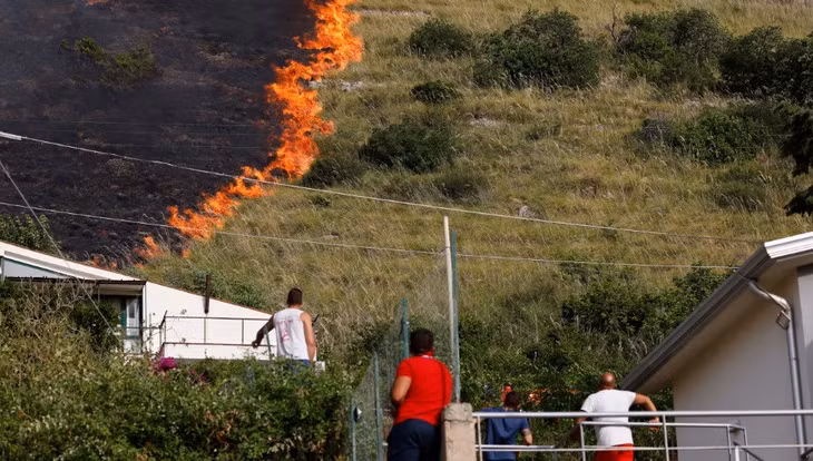 Người dân đứng xem ngọn lửa bùng cháy ở Capaci, gần Palermo, Sicily, Italy ngày 26/7. Ảnh: AFP