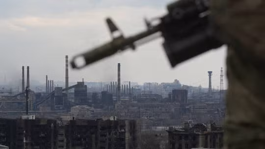 Quân nhân Nga cầm súng trường tấn công, phía xa là nhà máy thép Azovstal ở Mariupol. Ảnh: Sputnik