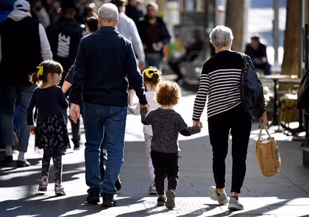 Trẻ em đi chơi cùng ông bà trên một đường phố ở Melbourne (Australia), ngày 28/6/2021. (Ảnh: AFP/TTXVN)