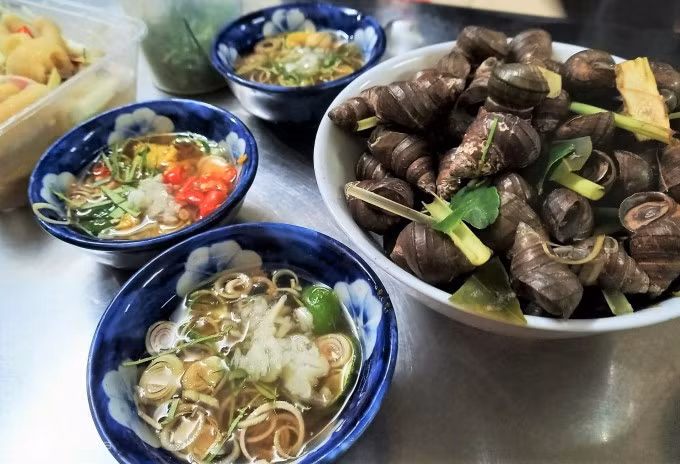 Ốc luộcĐây là món ăn vặt đơn giản nhưng có sức hấp dẫn kỳ lạ mỗi khi trời trở lạnh. Chiều tối được ngồi bên bát ốc luộc thơm phức mùi sả, chanh, gẩy con ốc bên trong ra dầm vào thứ nước chấm pha sẵn, vừa ăn vừa đưa đẩy câu chuyện bạn bè. Nước chấm chua cay, mặn, ngọt kèm thêm vài lát ớt, quất tươi quyện với cái giòn sật của con ốc nhỏ nóng hổi chính là hương vị của mùa đông giản dị. Hiện nay, các chủ hàng ngoài bán ốc luộc có thêm nhiều cách chế biến cũng như nguyên liệu đa dạng hơn từ xào me, sốt chanh dây, dùng thêm ngao sò, trứng cút... Bạn có thể tìm thấy các hàng ốc ngon ở những khu phố quanh Đại học Bách Khoa, Chùa Láng, Đình Ngang, Tôn Thất Tùng... Giá mỗi đĩa ốc luộc khoảng 20.000 - 50.000 đồng tùy loại. Ảnh: Khánh Trần