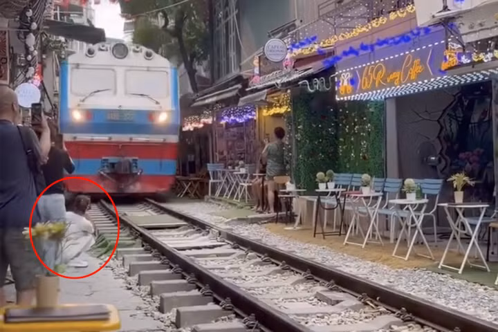 Cô gái ngồi sát đường ray tàu hỏa để ghi hình. (Ảnh cắt từ clip)