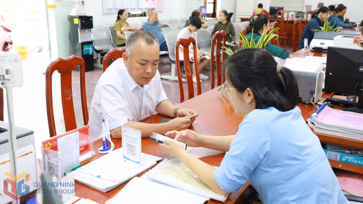 Cán bộ Trung tâm Phục vụ hành chính công phường Mạo Khê hướng dẫn người dân sử dụng điện thoại thông minh để thực hiện các quy trình giải quyết TTHC.