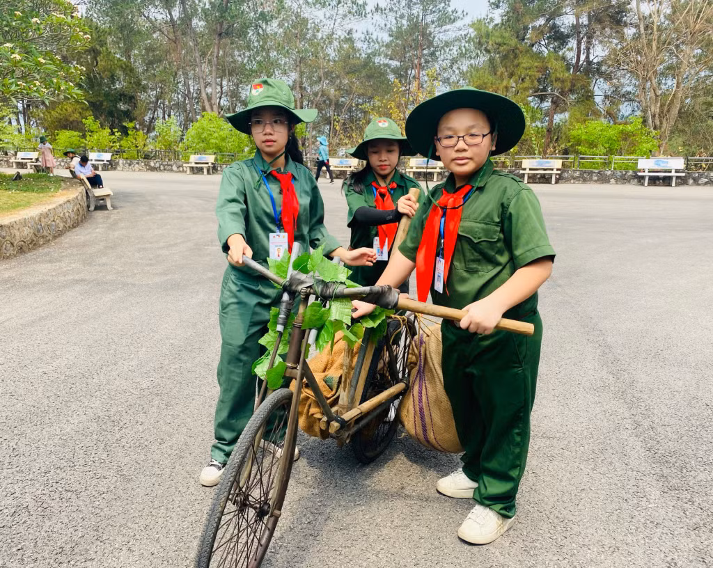 Các em tham gia trải nghiệm hóa thân thành những chiến sĩ quân đội đẩy xe đạp thồ trên đoạn đường dốc.