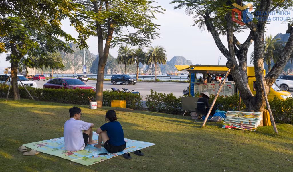 Đôi bạn trẻ tận hưởng buổi chiều êm đềm trên thảm cỏ xanh trong không gian khoáng đạt hướng ra Vịnh Hạ Long.