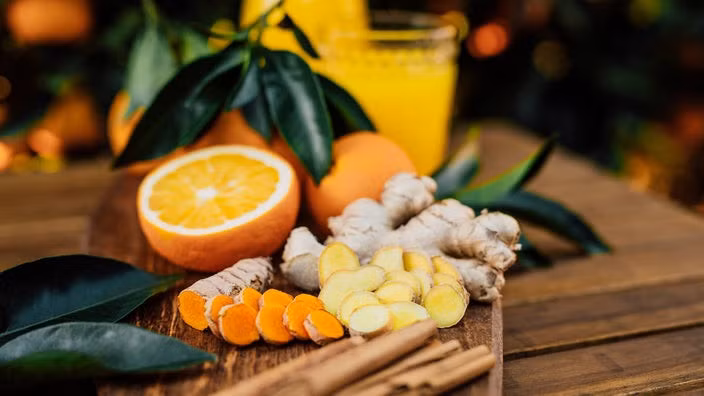 Nghệ tươi và gừng tươi cùng cam cắt đôi và quế xung quanh trên đĩa gỗ đẹp mắt trên bàn gỗ.