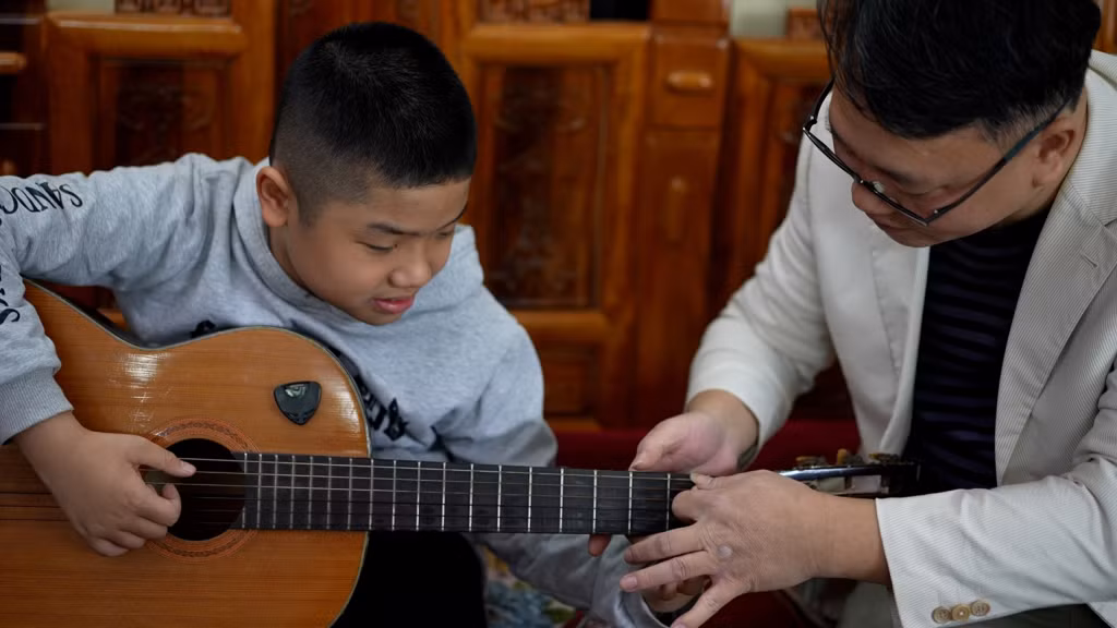 Nhạc sĩ Nguyễn Thiện Minh dạy chơi guitar cho một bạn nhỏ trong lớp học.