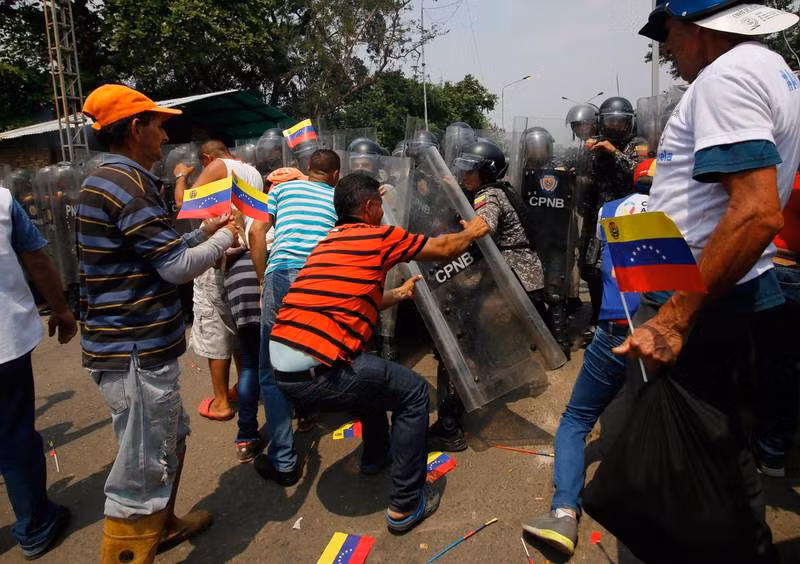 Số ủng hộ thủ lĩnh đối lập Juan Guaido đối mặt với cảnh sát đứng gác tại cây cầu đường bộ giáp ranh với Colombia. Ảnh: AFP